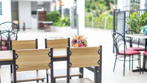 A restaurant with wooden chairs and tables, a floral centerpiece, and a view of greenery outside. - Tonsoi Hathairat (Bangkok)
