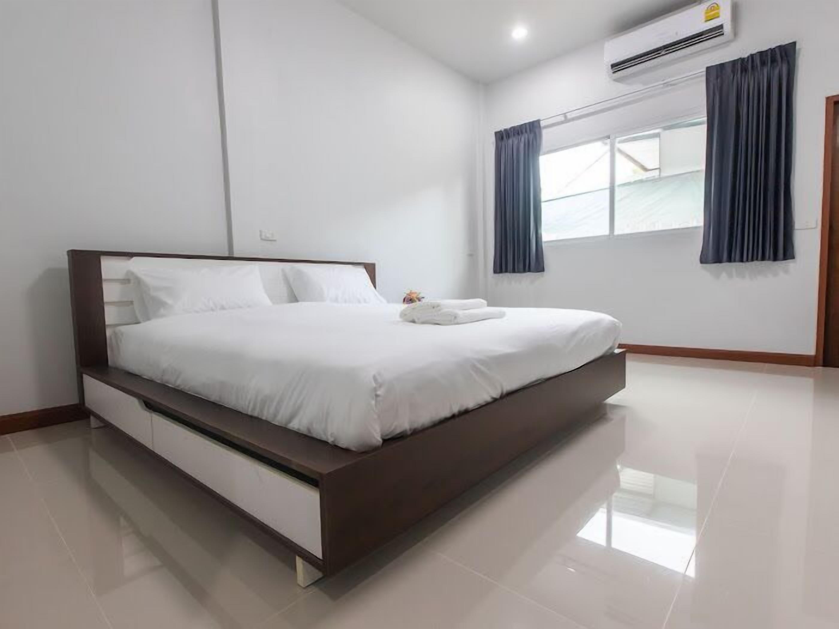 A modern bedroom with a large bed, white bedding, a wooden headboard, a built-in nightstand, and a window with curtains.