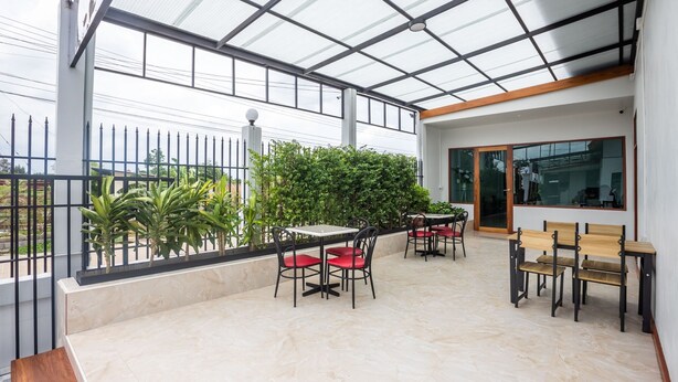 A covered outdoor seating area with tables and chairs, a tiled floor, and a view of the surrounding greenery and buildings. - Tonsoi Hathairat (Bangkok)