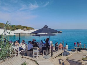Enjoy a meal with a view of the sea from our outdoor dining area, surrounded by lush greenery and a wooden deck.