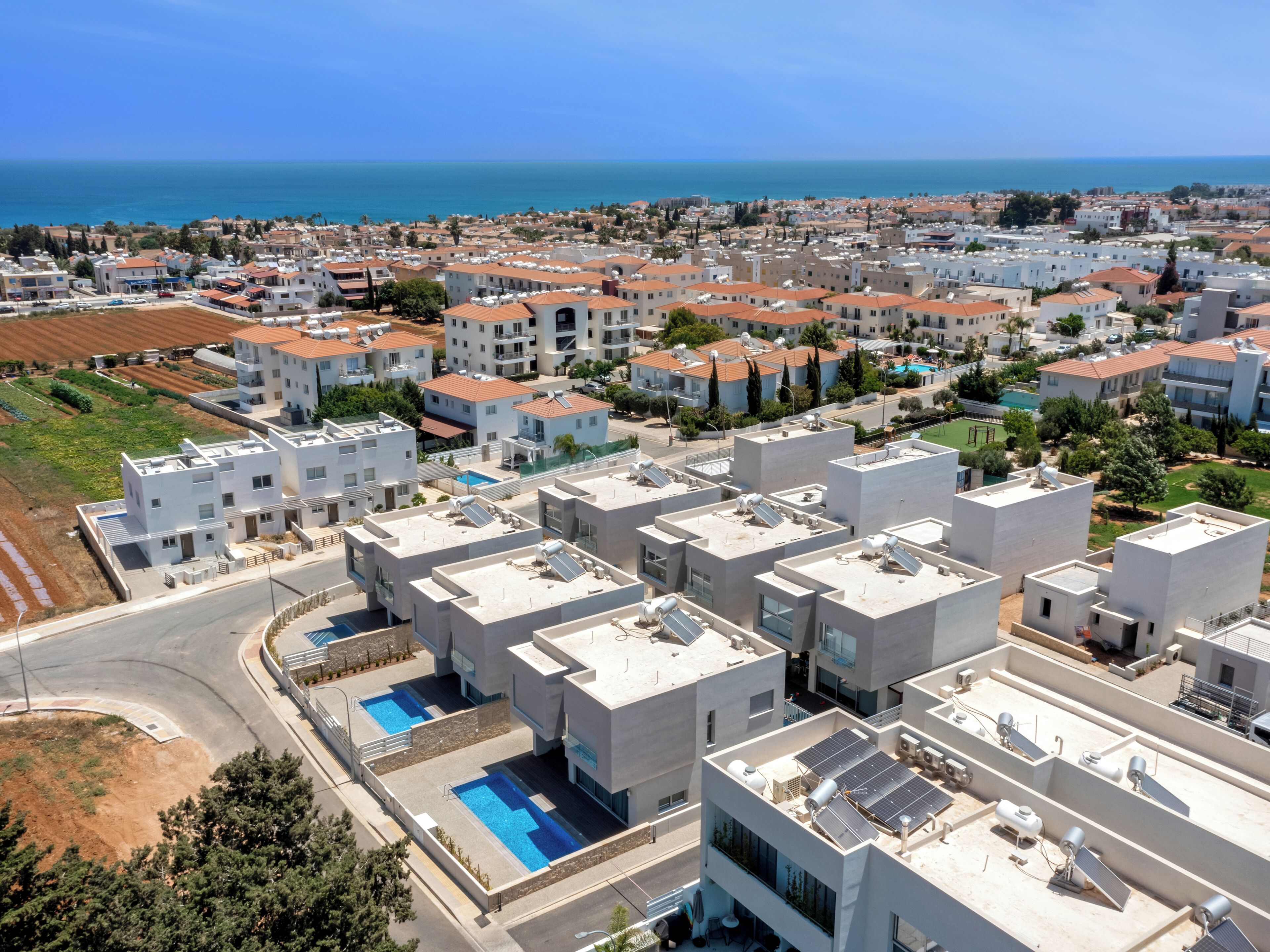 A residential area with modern buildings, a swimming pool, and a view of the sea.
