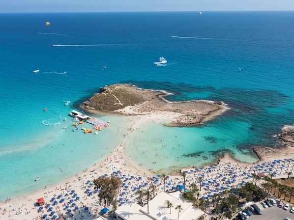 Relax on the beach with umbrellas and sun loungers at hand, surrounded by turquoise waters and a rocky outcrop.