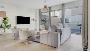 Un salon moderne avec un canapé gris, des fauteuils, un téléviseur à écran plat et une grande fenêtre avec des rideaux.