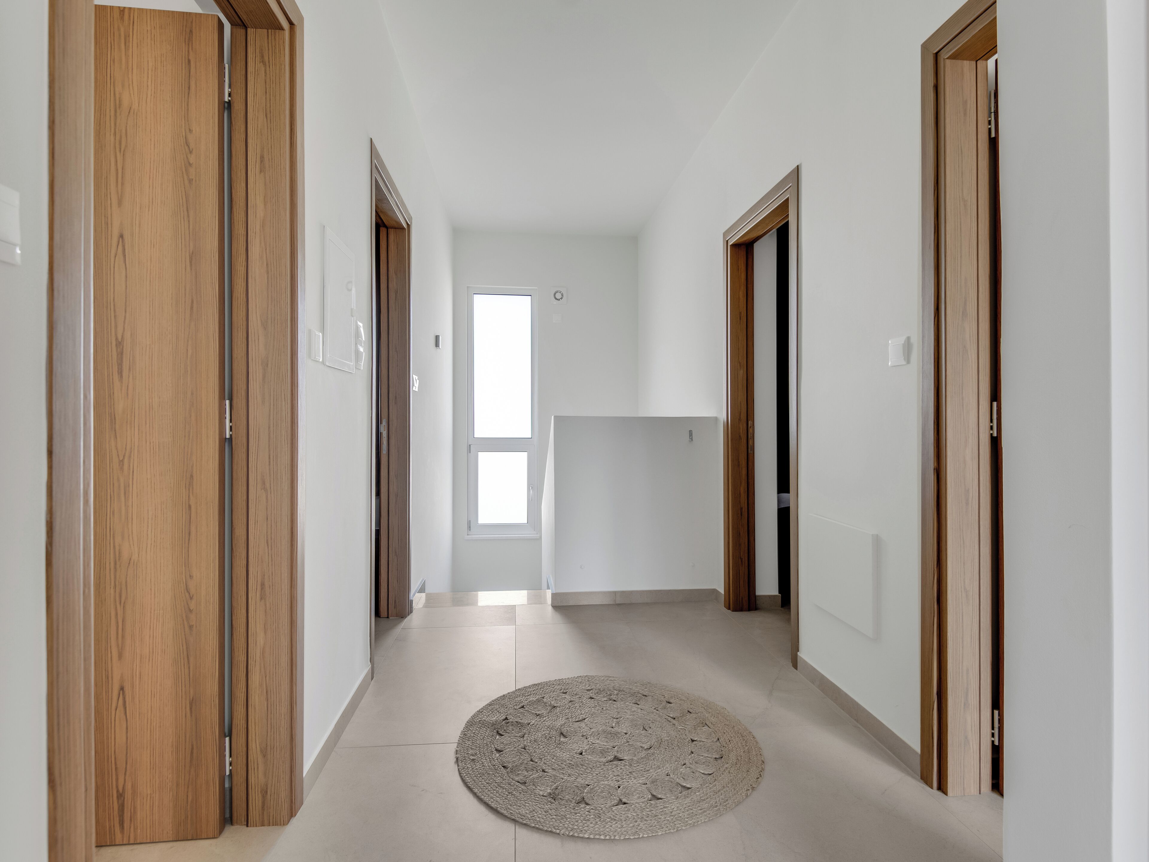 A hallway with wooden doors, a round rug, and a white wall.