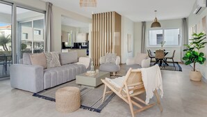 Un salon moderne avec un canapé gris, une table basse, un fauteuil en osier et un coin repas comprenant une table et des chaises.