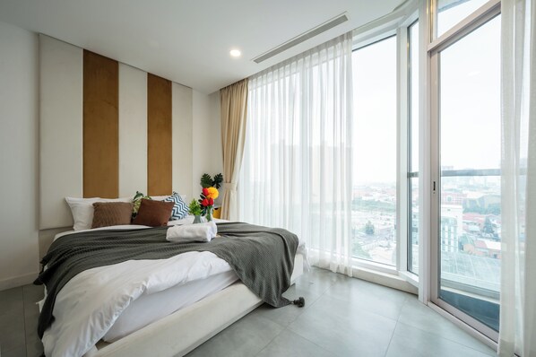A modern hotel bedroom with a large bed, a city view through floor-to-ceiling windows, and a minimalist decor.