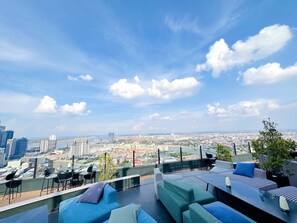 A rooftop terrace with outdoor seating, a view of a cityscape, and a river in the distance. - Penthouse Residence by Caerus Management (Phnom Penh)