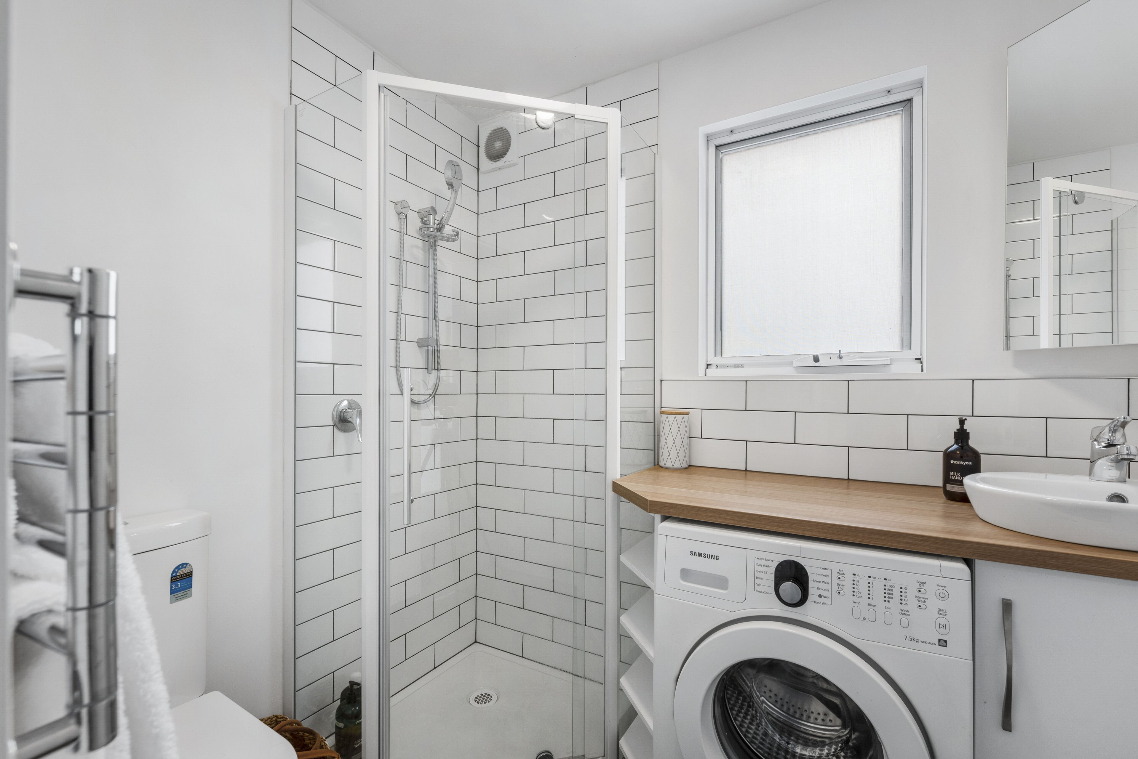 A modern bathroom with a shower, a washing machine, and a sink.