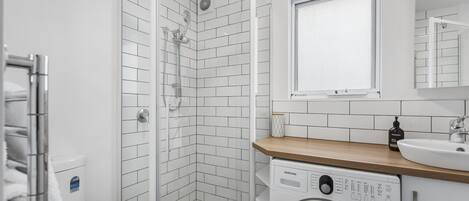 A modern bathroom with a shower, a washing machine, and a sink.
