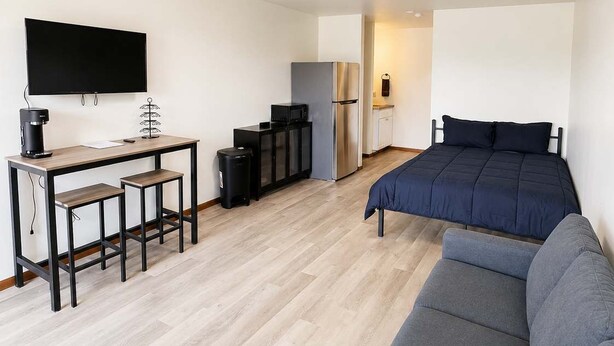 Une chambre moderne et minimaliste, équipée d’un canapé, d’une petite table avec une machine à café, d’une télévision, d’un réfrigérateur et d’un four à micro-ondes.