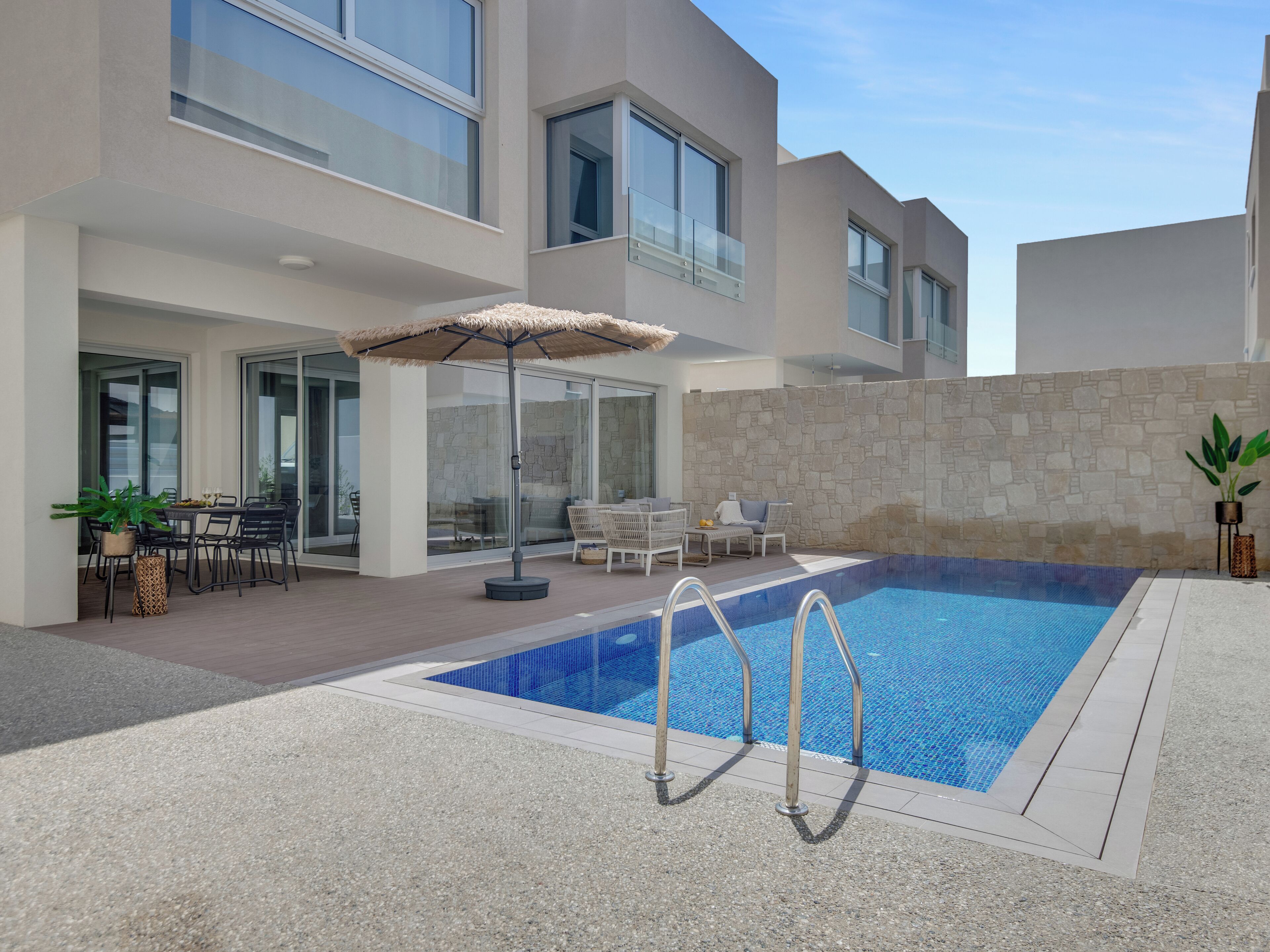 A modern outdoor pool area with a stone wall, lounge chairs, and a dining table with chairs.