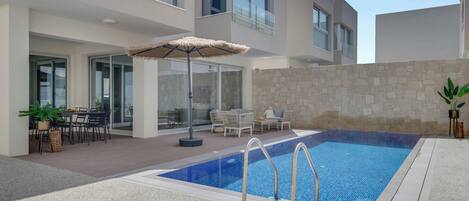 A modern outdoor pool area with a stone wall, lounge chairs, and a dining table with chairs.