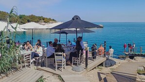 Een restaurant aan zee met terras, uitzicht op de zee, parasols en een houten terras.