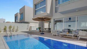 Een modern zwembadgedeelte met een helderblauw zwembad, buitenmeubilair en een glazen patio.