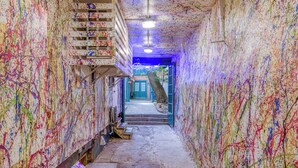 Ein schmaler Flur mit farbenfrohen Graffiti an den Wänden, einer Treppe und einer Tür am Ende.
