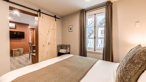 Ein Hotelzimmer mit einem großen Bett, einer Schiebetür, einem Fernseher, einem kleinen Tisch und Blick auf Gebäude.