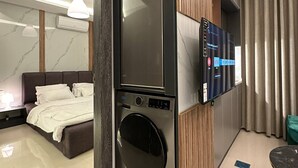 A modern hotel room with a built-in washer and dryer, a flat-screen TV, a bed, and a small dining area. - JRE Modern Apartment In Abdoun-amman (Amman)