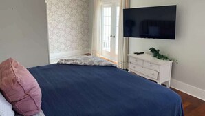 Une chambre à coucher avec un lit, une télévision, une commode et une fenêtre avec des rideaux.