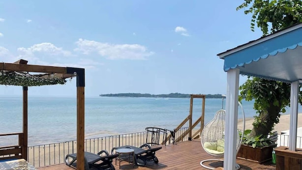 Une terrasse en bois avec des sièges d’extérieur, un fauteuil suspendu et une vue sur la mer.