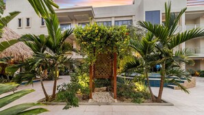 Ein Innenhof mit einer Holzpergola, Palmen und einer Struktur mit einem Reetdach.