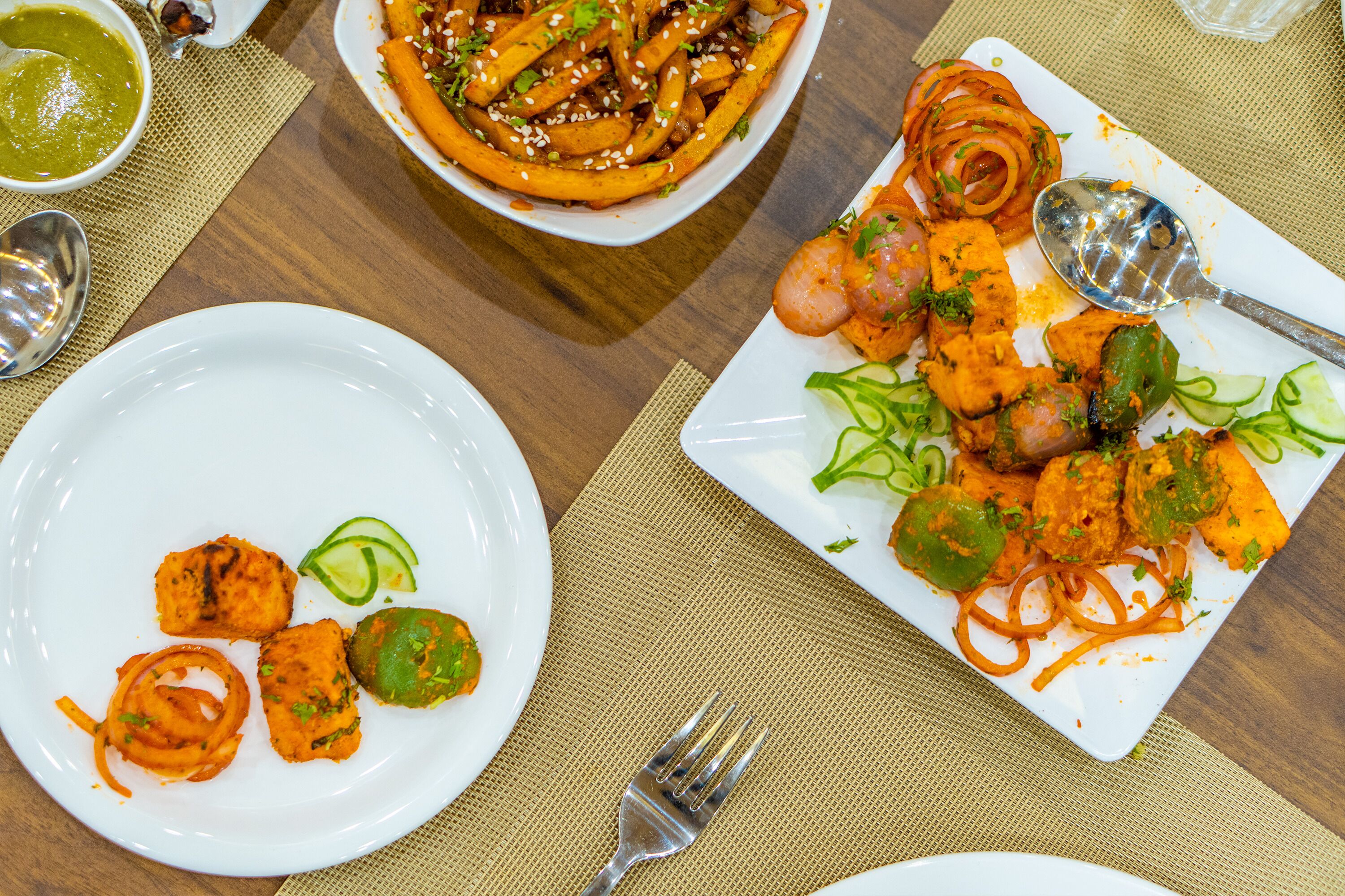 A table with various dishes, including a bowl of soup, a plate of fries, and a plate with shrimp and vegetables.