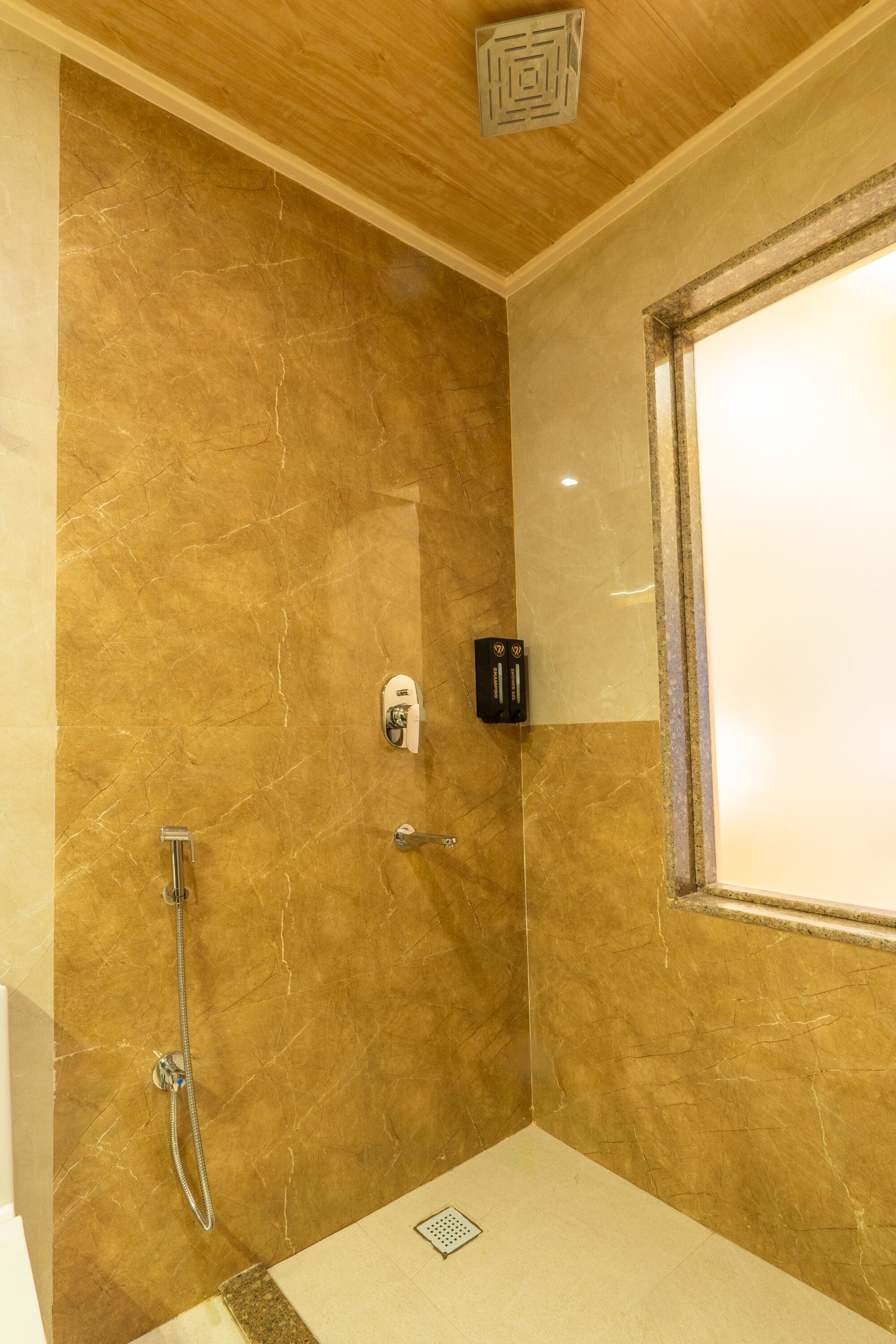 A shower with a marble wall, a handheld showerhead, and a wall-mounted control panel.