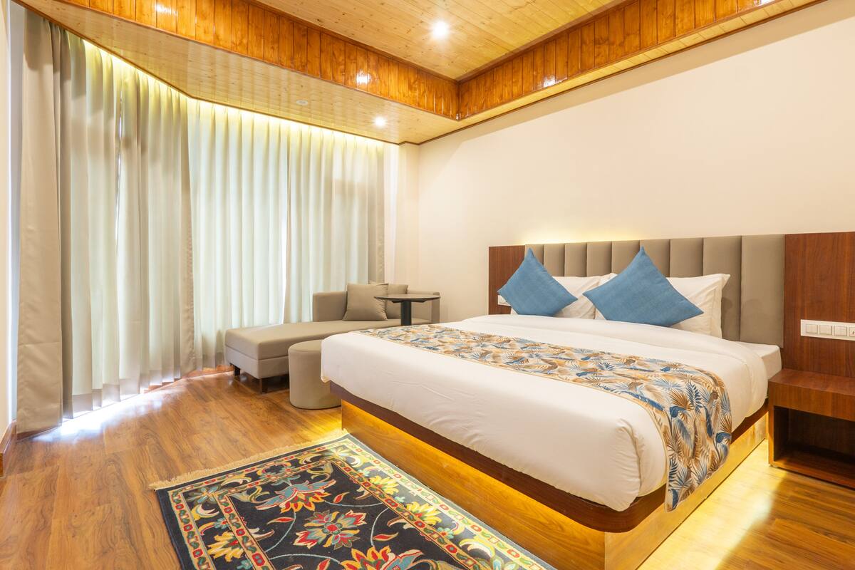 Een hotelkamer met een groot bed, een kleine zithoek, een nachtkastje en een houten plafond.