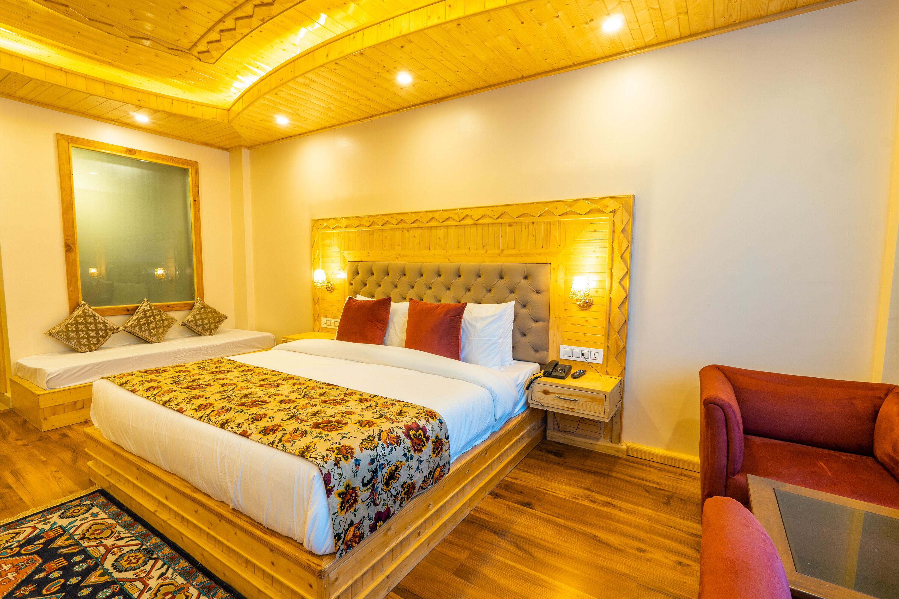 A hotel room with a large bed, a wooden headboard, a nightstand, a red armchair, and a wooden floor.