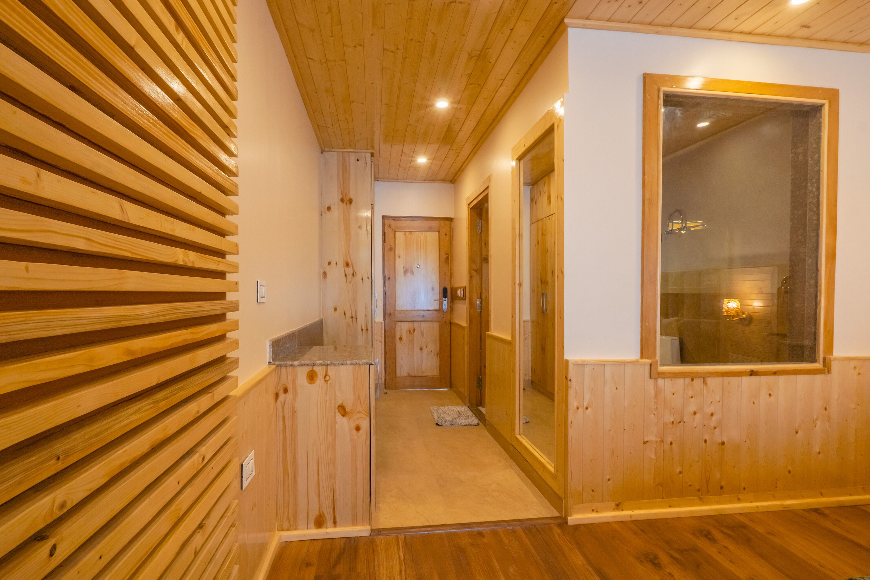 Un pasillo interior de madera con un revestimiento de listones de madera, una puerta que da a un baño y un ventanal grande.