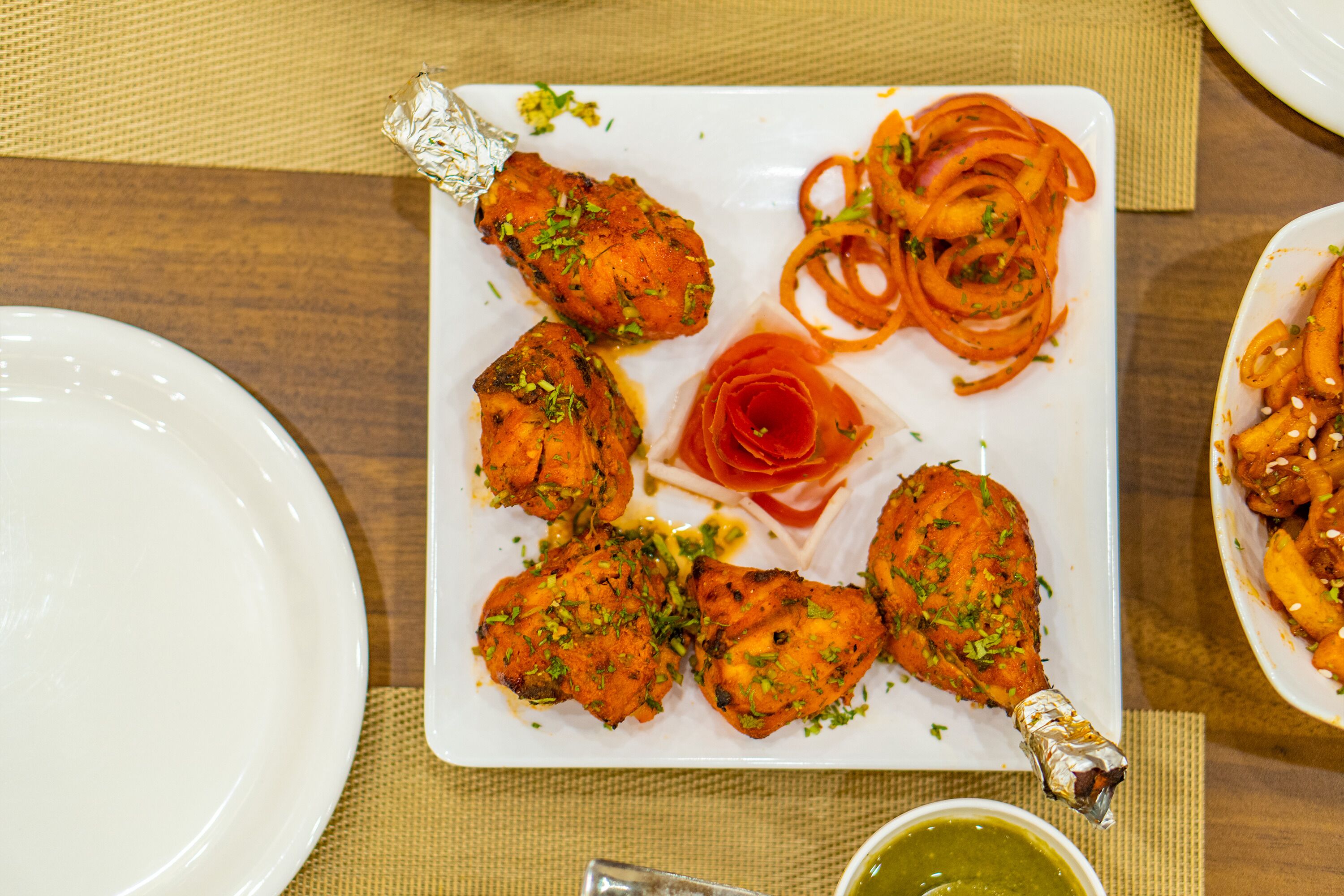 A plate of tandoori chicken with vegetables and a side of sauce.