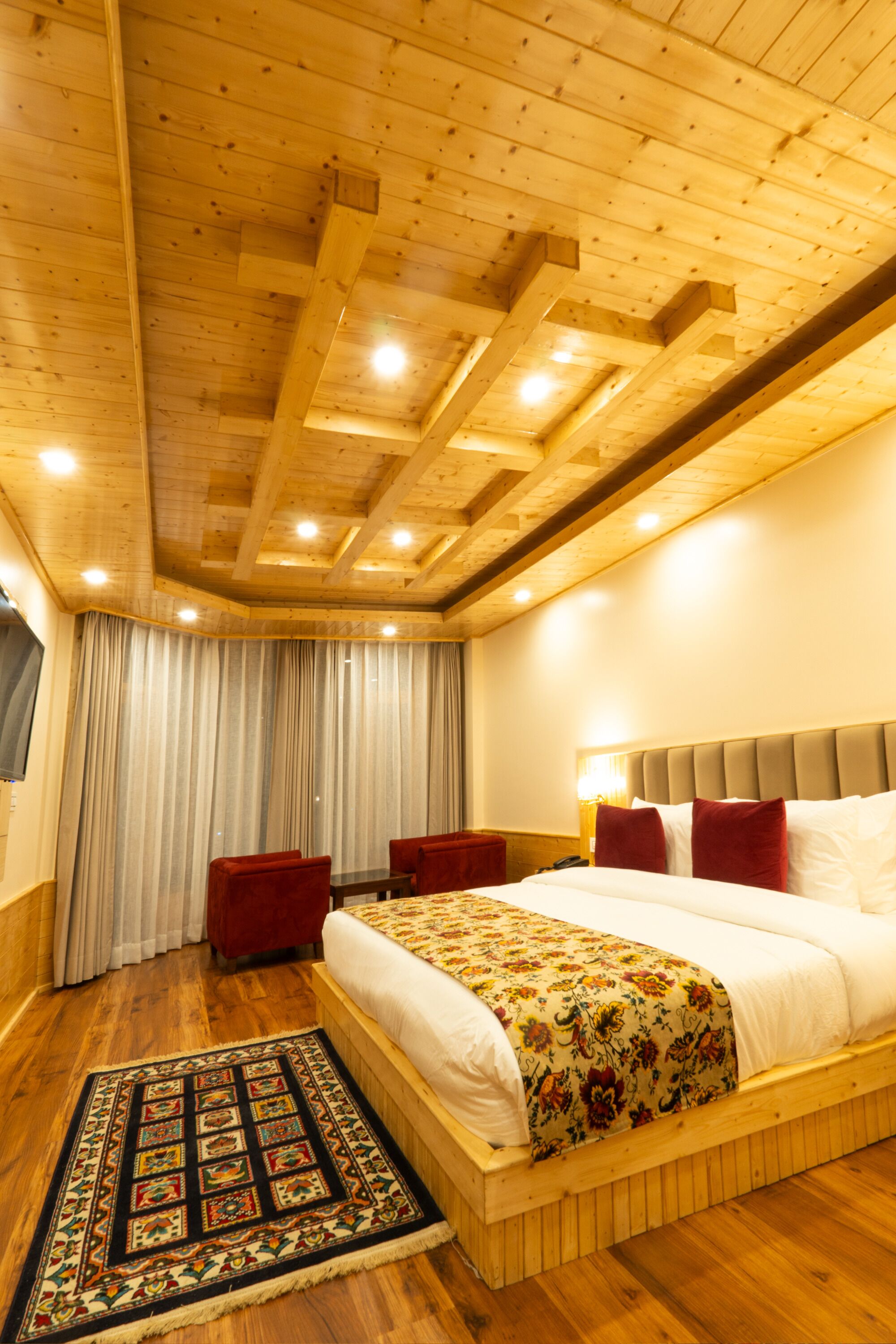 A wooden-paneled bedroom with a large bed, a red chair, and a patterned rug.