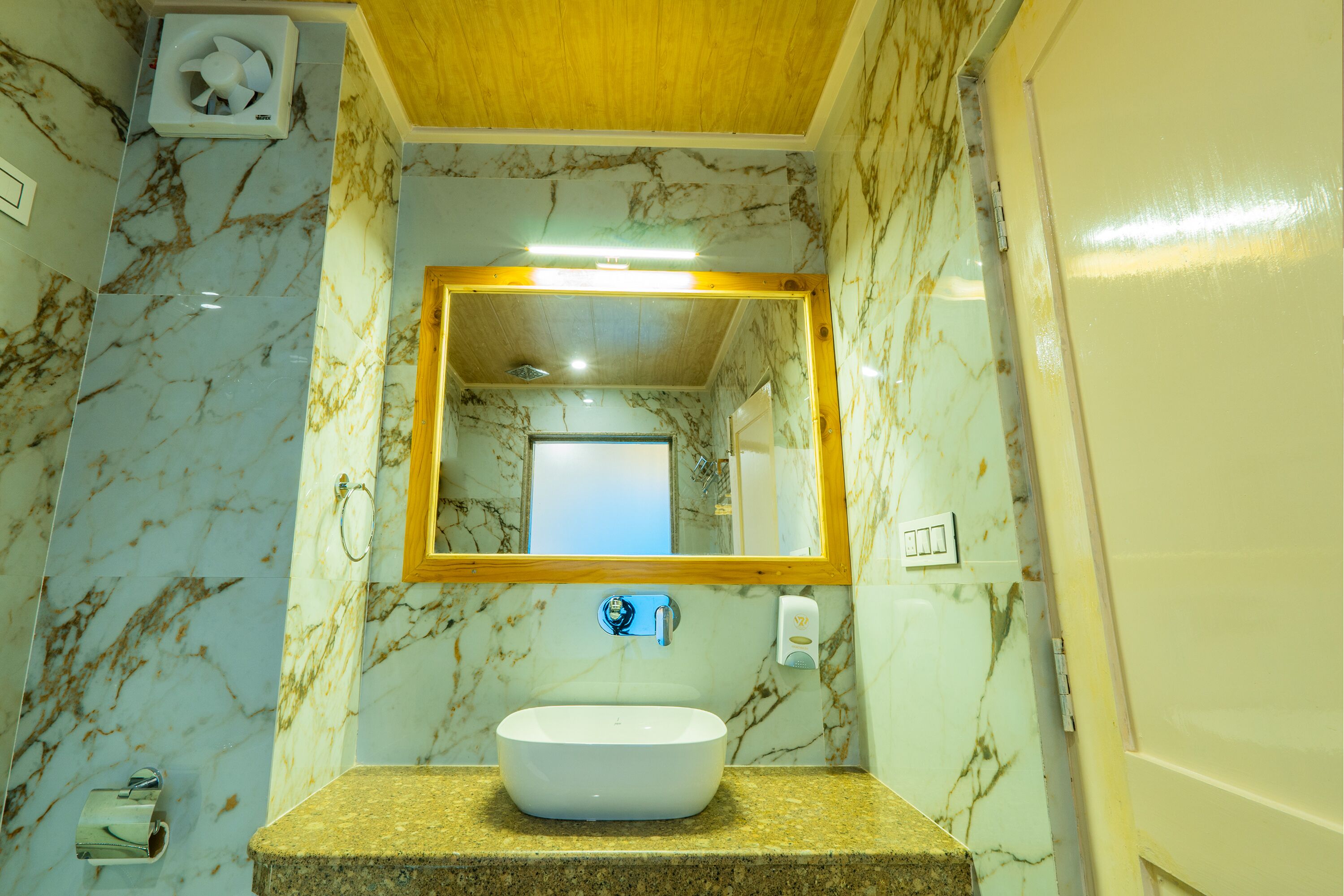 Un bany amb paret de marbre, un lavabo, un mirall i un ventilador al sostre.