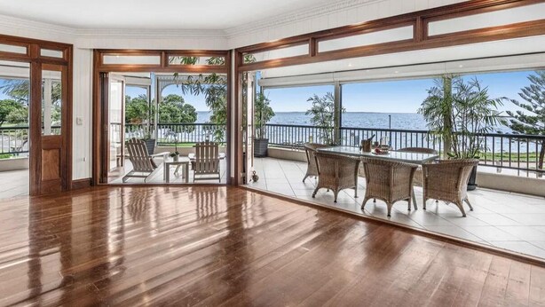 Amplia habitación con piso de madera, balcón con mobiliario de mimbre y vista al mar.