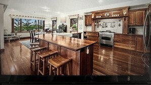 Una cocina amplia con armarios de madera, una isla central con taburetes y un ventanal con vistas a la vegetación.