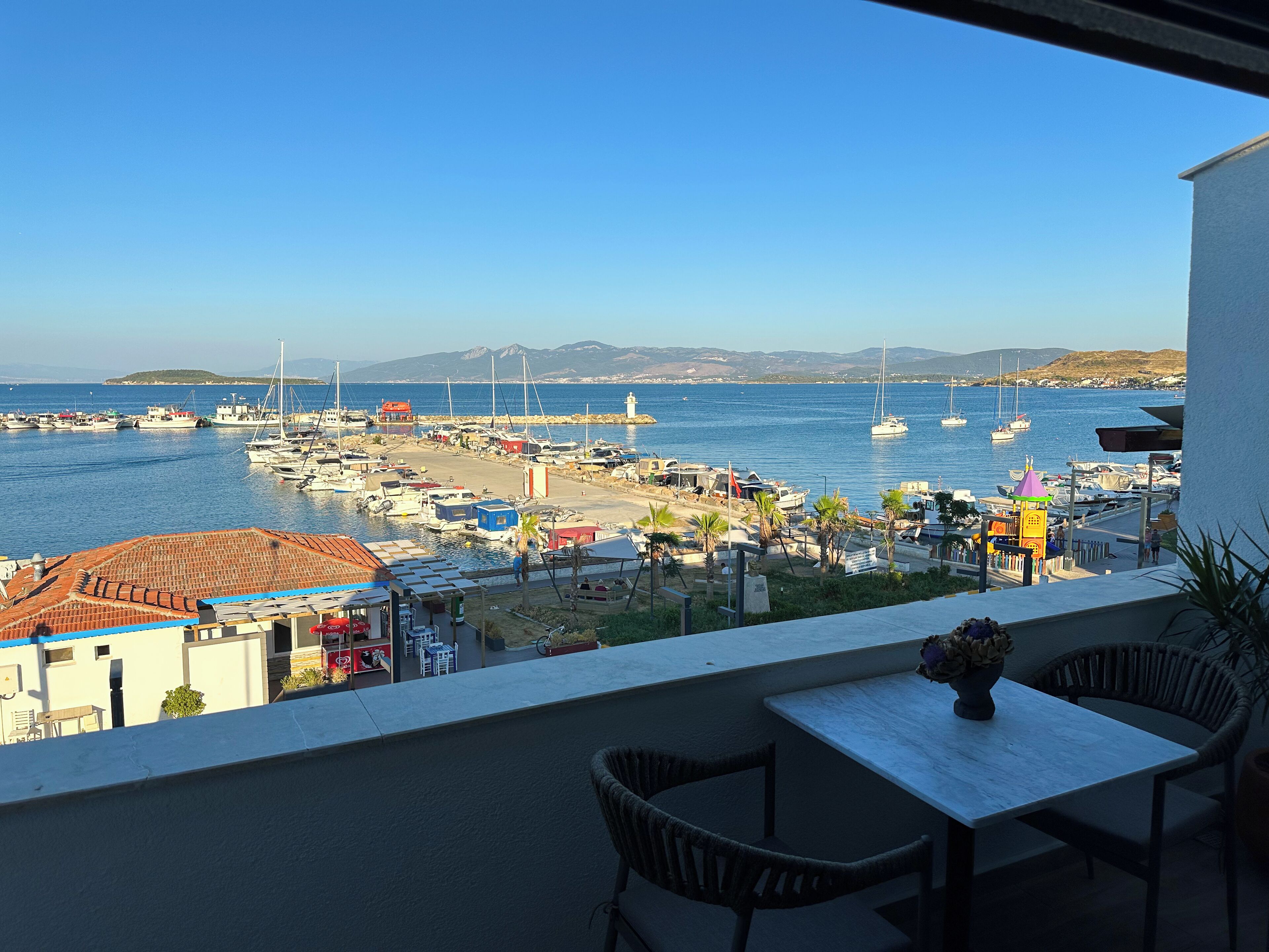 Un balcon offrant une vue sur un port de plaisance, des bateaux et des montagnes lointaines.