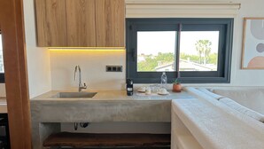 A compact kitchen with a built-in sink, wooden cabinets, a window with a view, and a small countertop with a potted plant. - Donmez Otel (Urla)