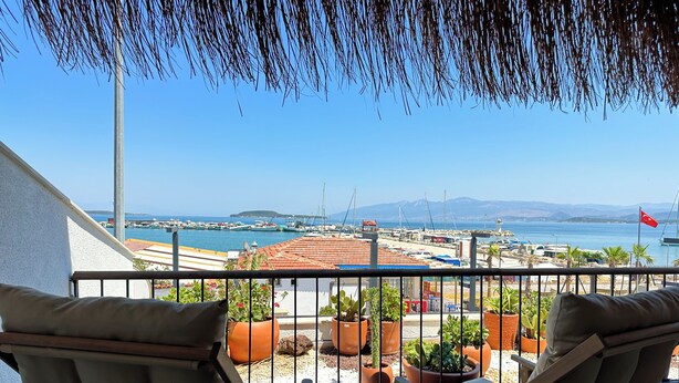 A balcony with two wooden chairs and potted plants, overlooking a marina with boats and a distant island. - Donmez Otel (Urla)
