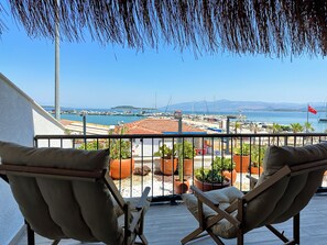 A balcony with two wooden chairs and potted plants, overlooking a marina with boats and a distant island. - Donmez Otel (Urla)