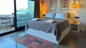 A bedroom with a bed, a nightstand, a chair, a table, and a view of the sea. - Donmez Otel (Urla)