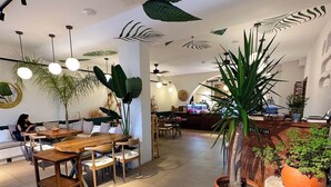 A modern interior with a dining area, multiple tables, chairs, and potted plants. - Donmez Otel (Urla)