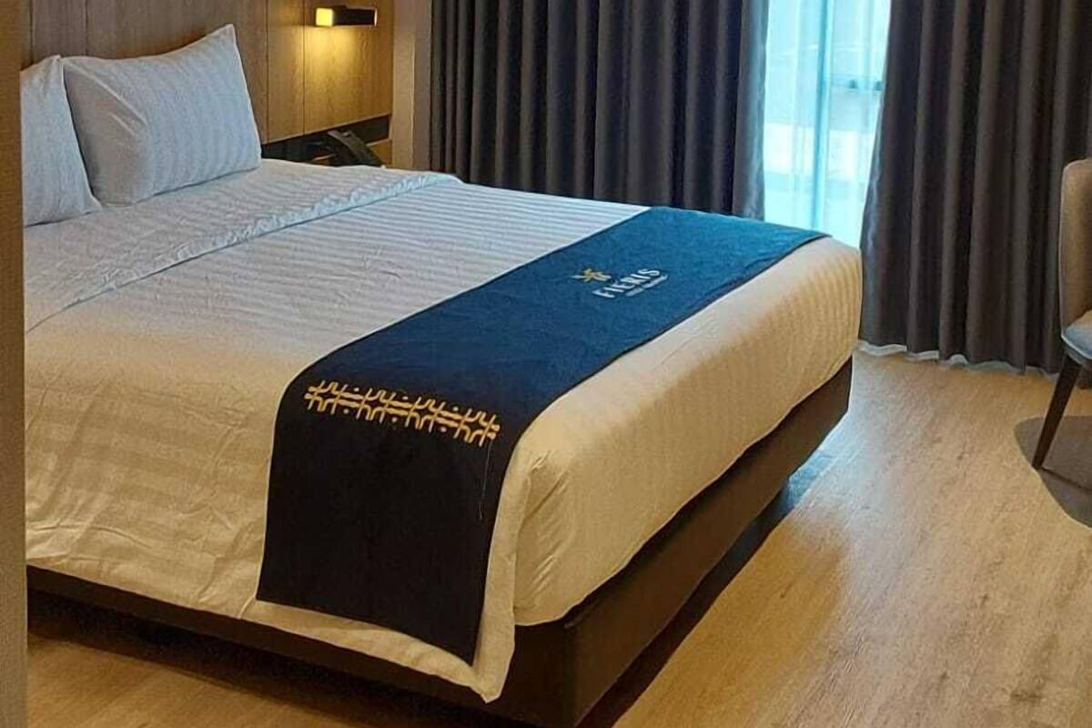 Une chambre d’hôtel avec un grand lit, une table de chevet, une chaise et une fenêtre avec des rideaux.
