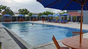 Une piscine entourée d’un petit muret et agrémentée de plantes en pot, avec des chaises longues et des parasols à proximité.