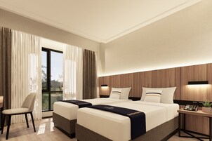 Ein modernes Hotelzimmer mit einem großen Bett, zwei Nachttischen, einem Sessel und Blick ins Freie.
