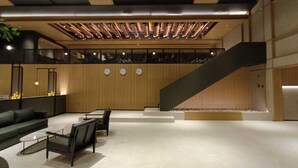 Un hall d’entrée moderne avec un escalier, un espace salon et un mur en bois orné d’horloges.
