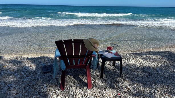 Een strand met een stoel en een tafel op kiezels, uitkijkend over de oceaan.