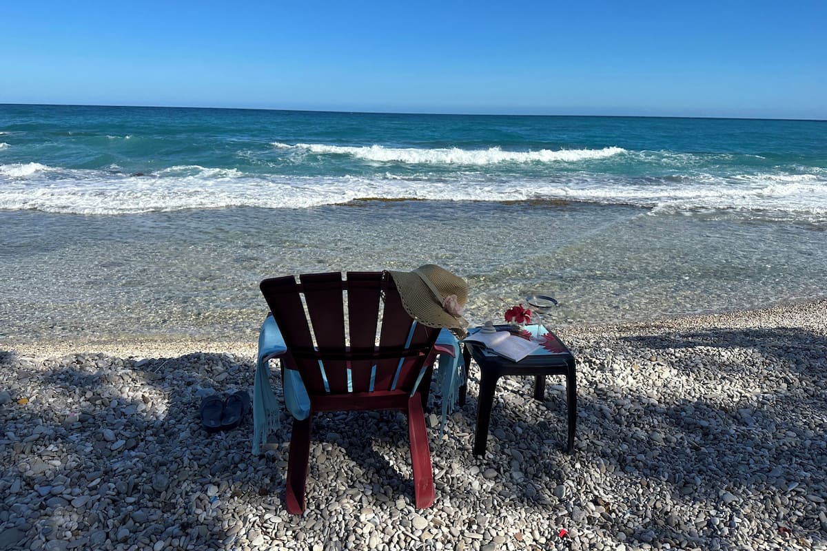 Ein Strand mit Stuhl und Tisch, aufgeständert auf Kieselsteinen, mit Blick aufs Meer.