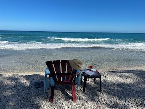 A beach with a chair and a table set up on pebbles, facing the ocean.