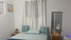 Een slaapkamer met een bed, nachtkastje, kapstok, spiegel en raam met zonwering.