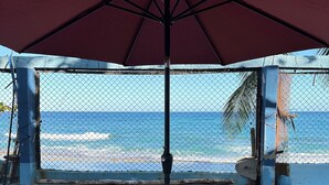 Uitzicht op de oceaan vanaf een overdekt terras met twee rode stoelen en een grote parasol.