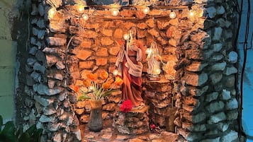 Un nicho de pared de piedra con una estatua de Jesús Cristo, una pequeña estatua de la Virgen María y un florero con flores.